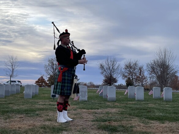 A bagpiper at Iowa Veterans cemetery silhouetted against a morning sky